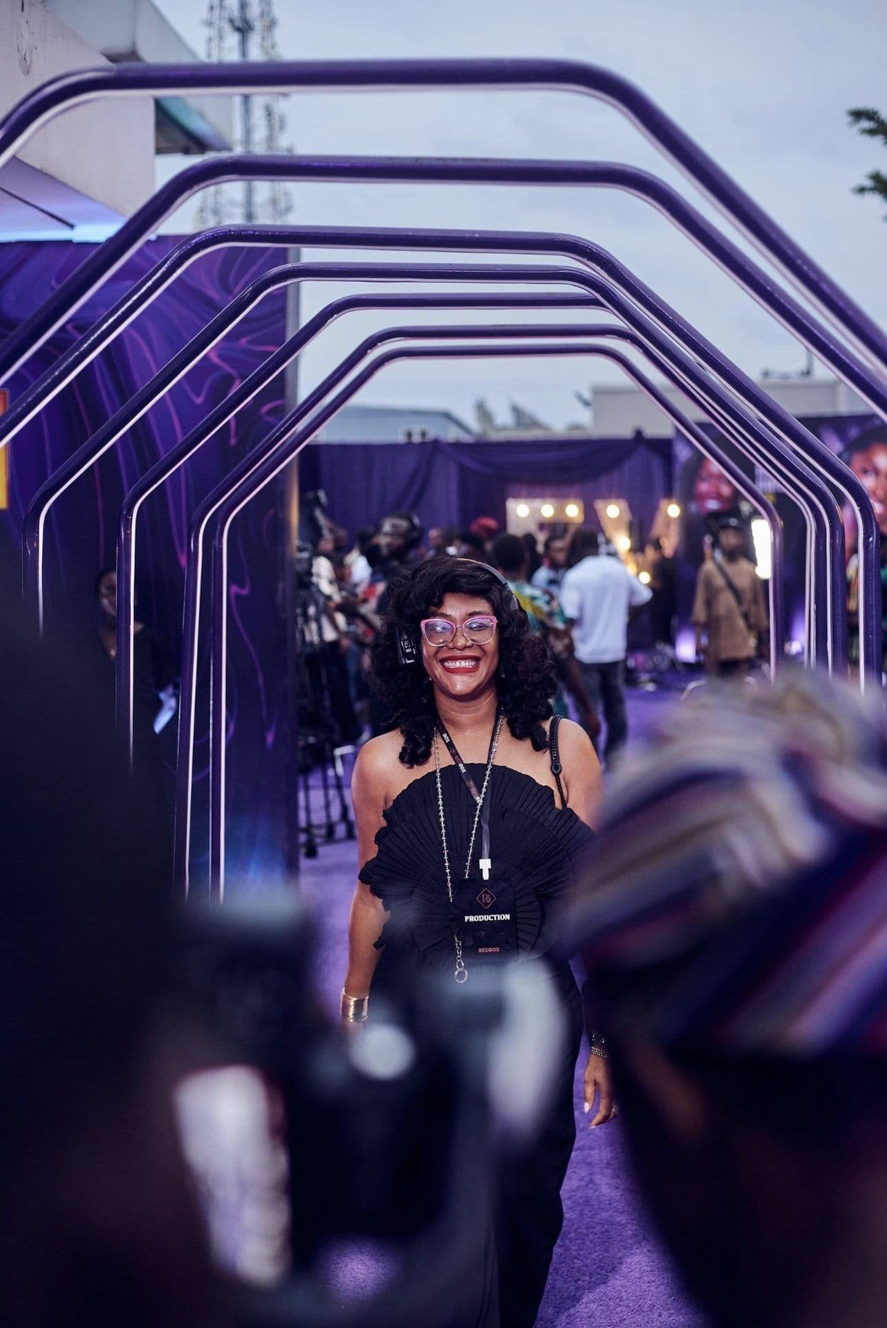 Amaka on headset, running the show on a purple carpet